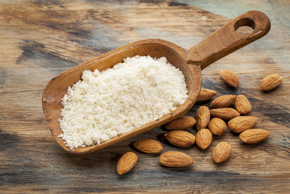 Poudre d'amande dans une cuillère en bois et amandes entières