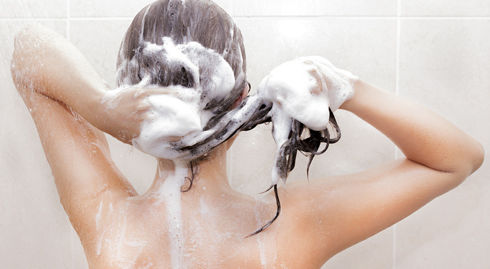 Femme nue sous la douche se lavant les cheveux