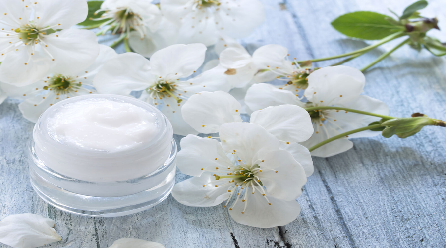 Un pot de crème hydratante maison avec des fleurs blanches à côté