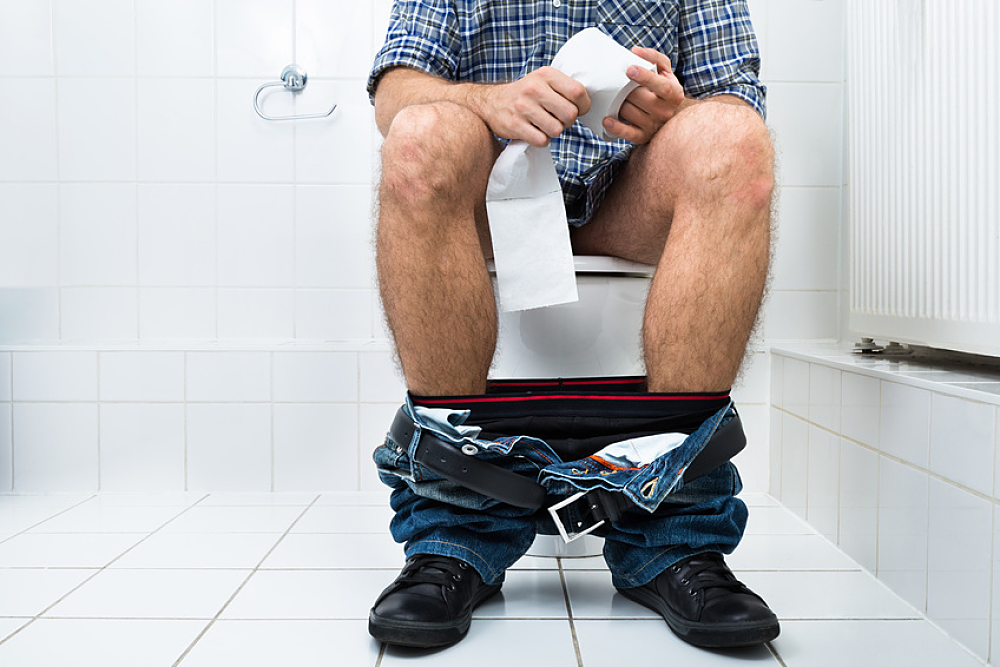 homme assis sur les toilettes tenant un rouleau de papier dans les mains