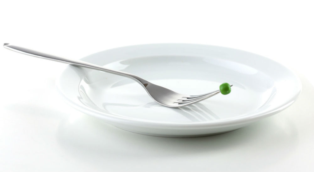 Assiette vide et petit pois au bout d'une fourchette