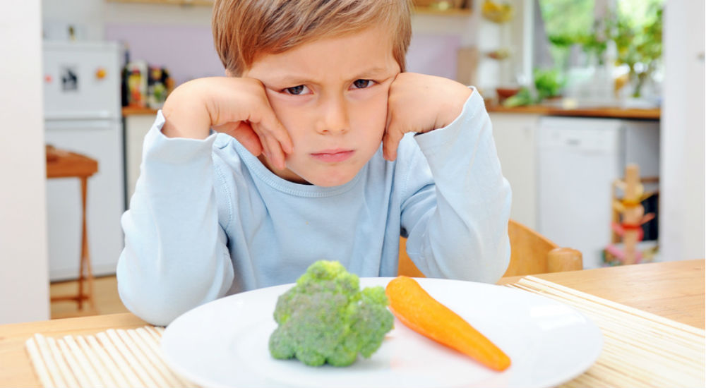 Enfant qui boude devant une assiette de légume
