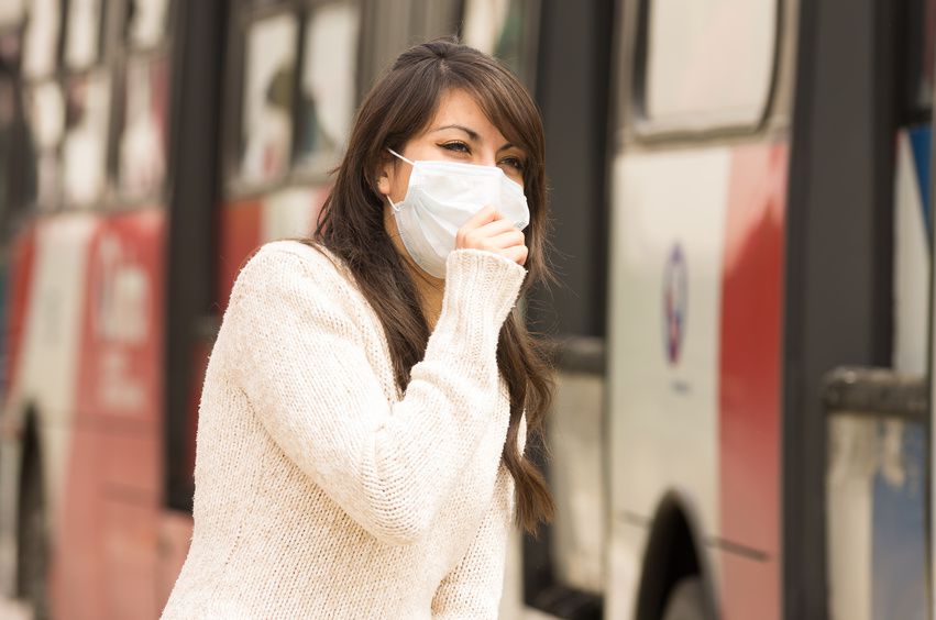 Une femme avec un masque se promène près d'un bus en ville