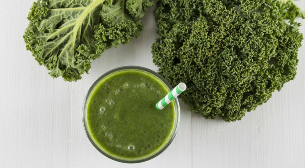 Un verre de jus de chou frisé et quelques branches à coté.