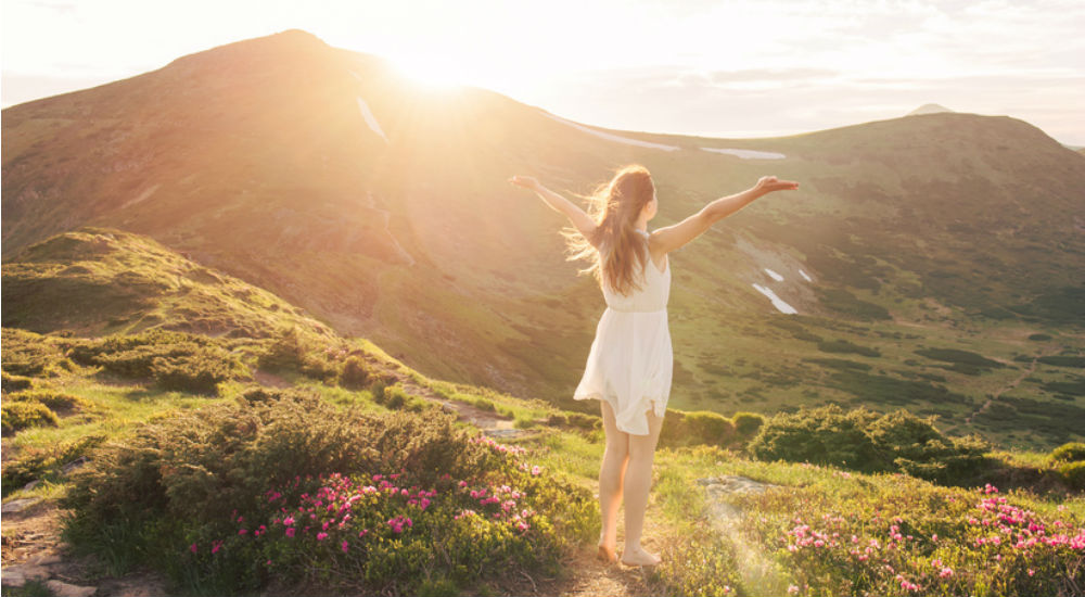 femme en robe blanche dans la nature face à un lever de soleil