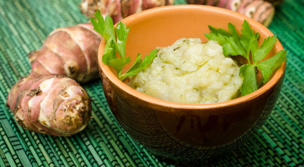 Un bol de purée de topinambours et quelques topinambours à côté.