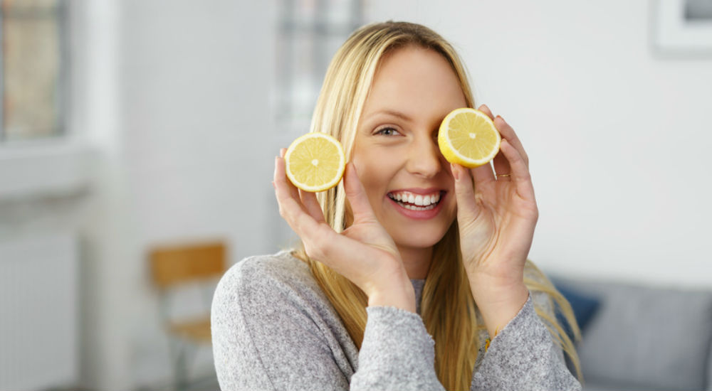 Une femme mince tient deux morceau de citron à la main et fait un clin d'oeil avec l'un des morceaux.