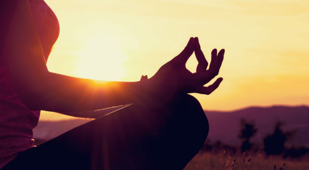 une femme médite devant un coucher de soleil