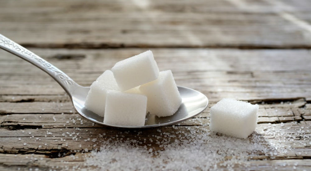 du sucre dans une cuillère à café sur une table en bois