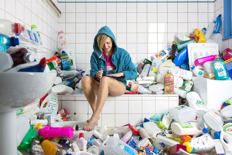 Une femme se vernie les ongles dans une salle de bain encombrée de bidons de lessives