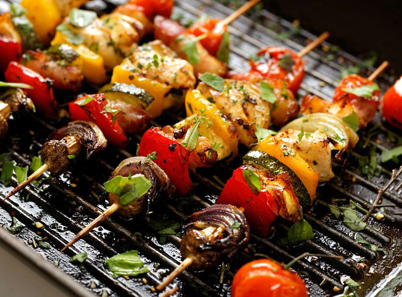 4 brochettes de légumes en train de cuire sur une grille de barbecue