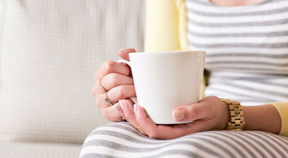 une femme tient une boisson chaude dans une tasse blanche