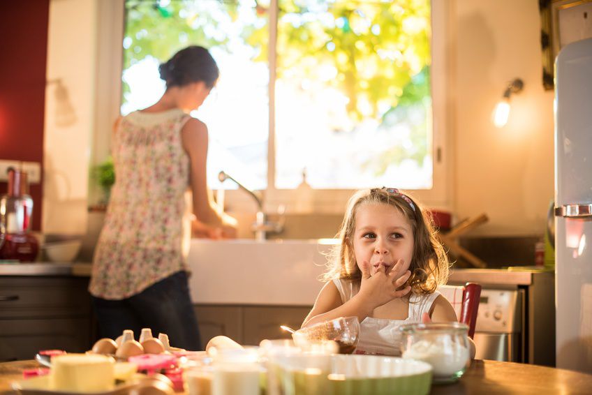 une petite fille mange de la pâte à gâteau pendant que sa mère a le dos tourné