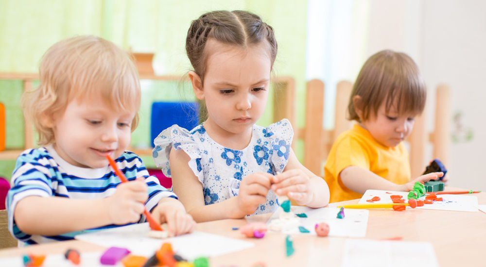 trois enfants en train de jouer avec de la pâte à modeler sur une table