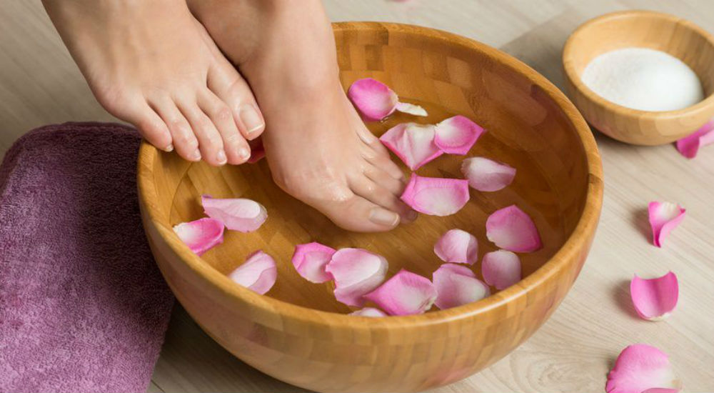 des pieds de femme qui trempent dans de l'eau contenant des pétales de roses