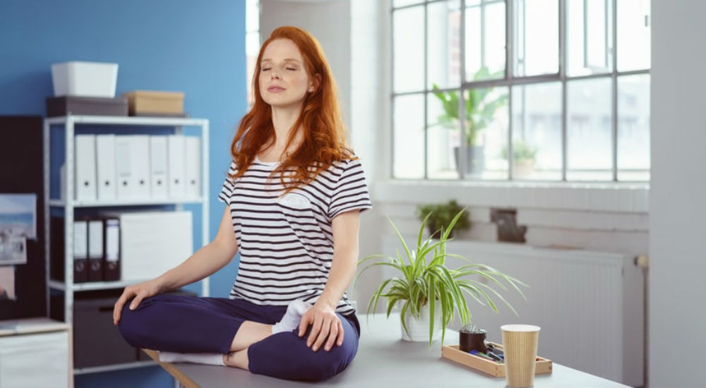 une femme zen médite sur son bureau de travail