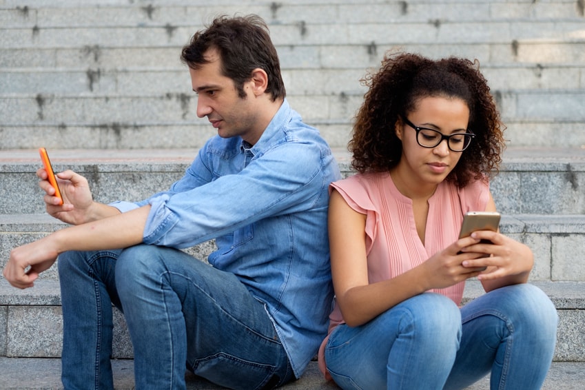 deux personnes qui se tiennent dos à dos et qui regardent leur portable