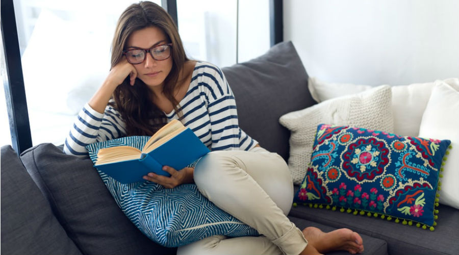 une femme lit un livre sur son canapé